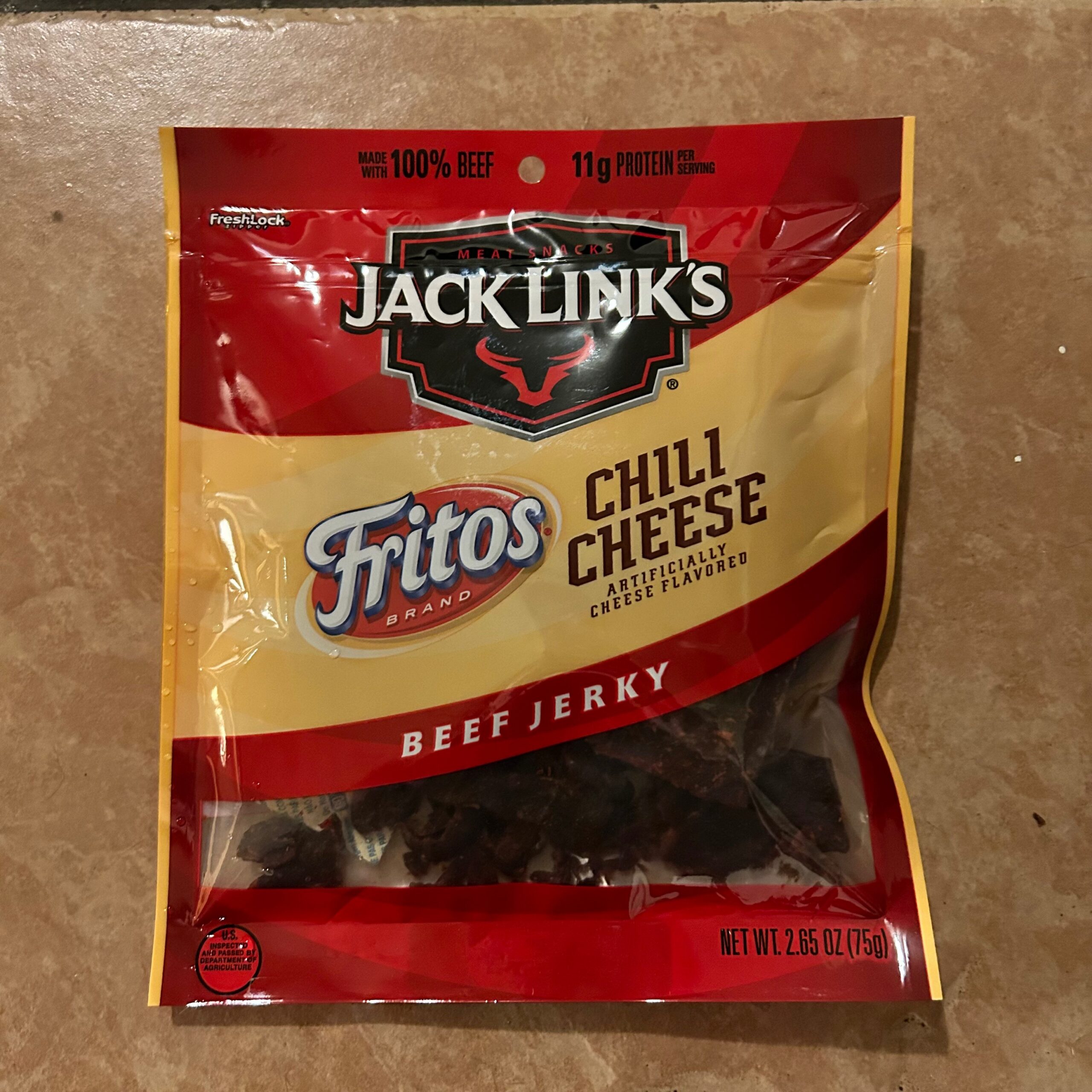 A brown background with a bag of Jack Link's jerky. The jerky bag reads Jack Link's Frito's Chili Cheese artificially flavored cheese beef jerky.